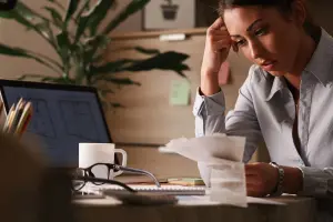 Mulher preocupada analisando contas e boletos, representando a frustração causada por cobranças indevidas e a busca por soluções jurídicas para resolver o problema.