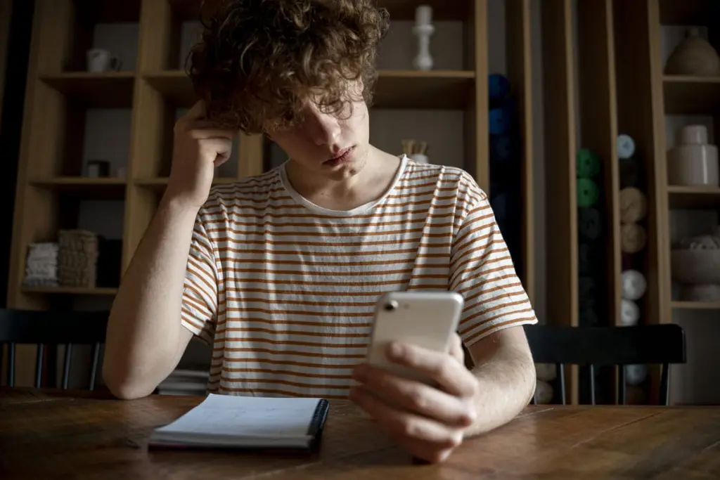 Jovem preocupado olhando para o celular, representando dúvidas sobre pensão alimentícia, direito ao benefício e revisão dos valores.