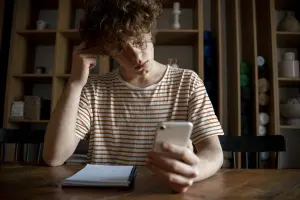 Jovem preocupado olhando para o celular, representando dúvidas sobre pensão alimentícia, direito ao benefício e revisão dos valores.